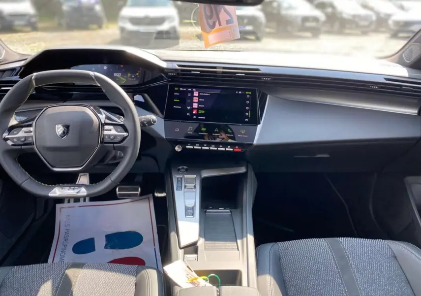 Vue intérieure avant de la Peugeot 308 2025 gris selenium, mettant en valeur le volant compact et l'écran tactile central moderne.