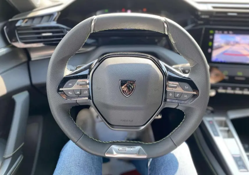 Volant sport GT de la Peugeot 308 2025 en vue plongeante, avec commandes intégrées et coutures vertes visibles.