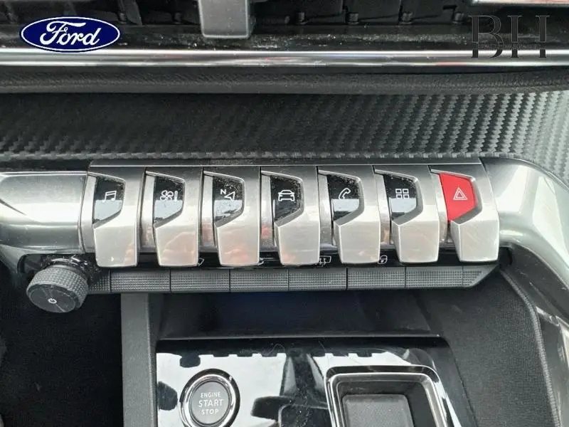 Gros plan sur la rangée de boutons métalliques du tableau de bord du Peugeot 5008 gris Platinium, avec bouton rouge d'alerte.