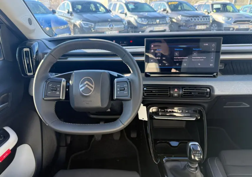 Vue intérieure centrée sur le volant et tableau de bord de la Citroën C3 gris 2025 avec écran tactile et boîte manuelle.