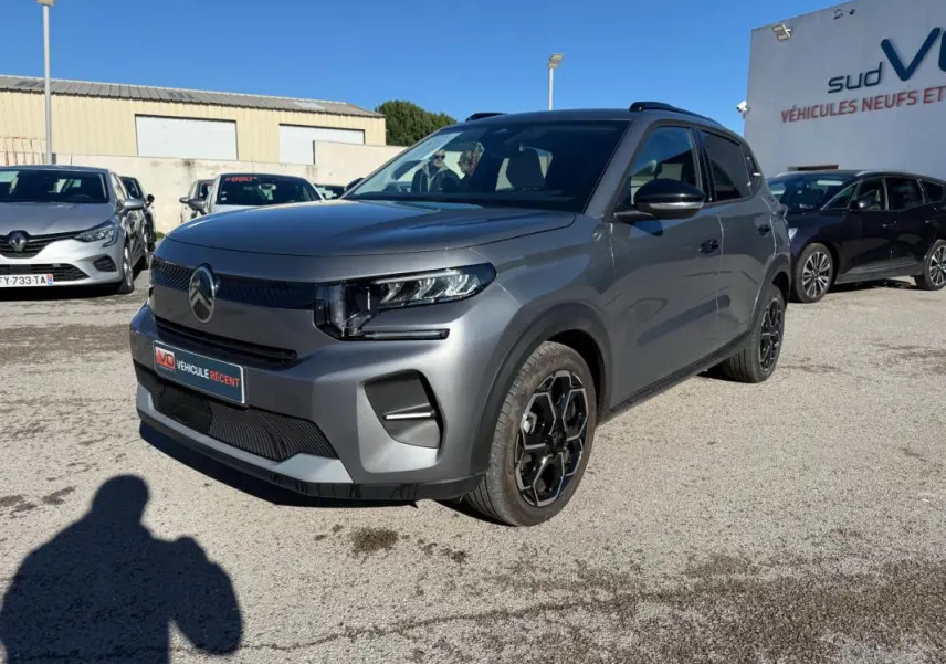 Vue 3/4 avant droite d'une Citroën C3 gris métallisé avec jantes alliage noires et barres de toit visibles.
