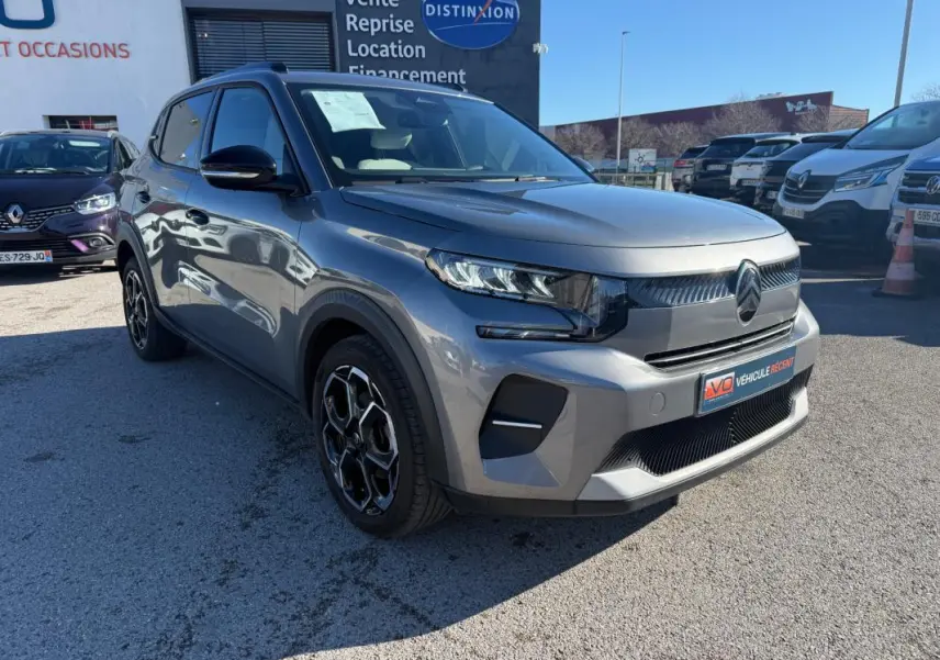 Vue 3/4 avant droite d'une Citroën C3 gris métallisé 2025 avec jantes alliage 17 pouces et barres de toit.