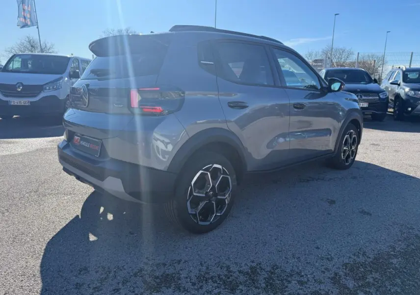 Citroën C3 gris vue 3/4 arrière droit, avec barres de toit et jantes alliage 17 pouces sous un ciel bleu.