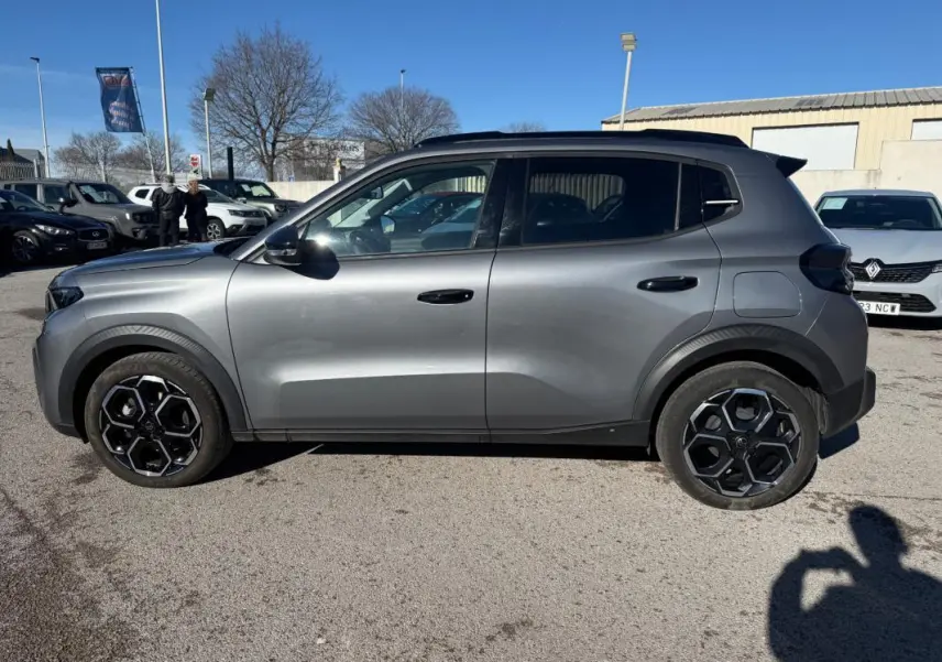 Vue de profil côté gauche d'une Citroën C3 gris 2025 avec jantes alliage noires et barres de toit visibles.