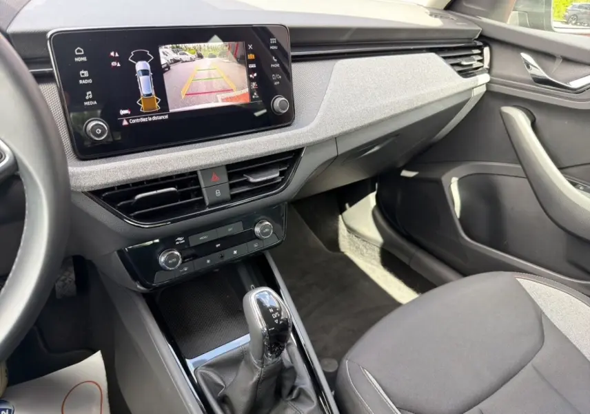 Vue intérieure côté passager de la Skoda Scala gris foncé, avec écran tactile affichant la caméra de recul et levier de boîte auto.