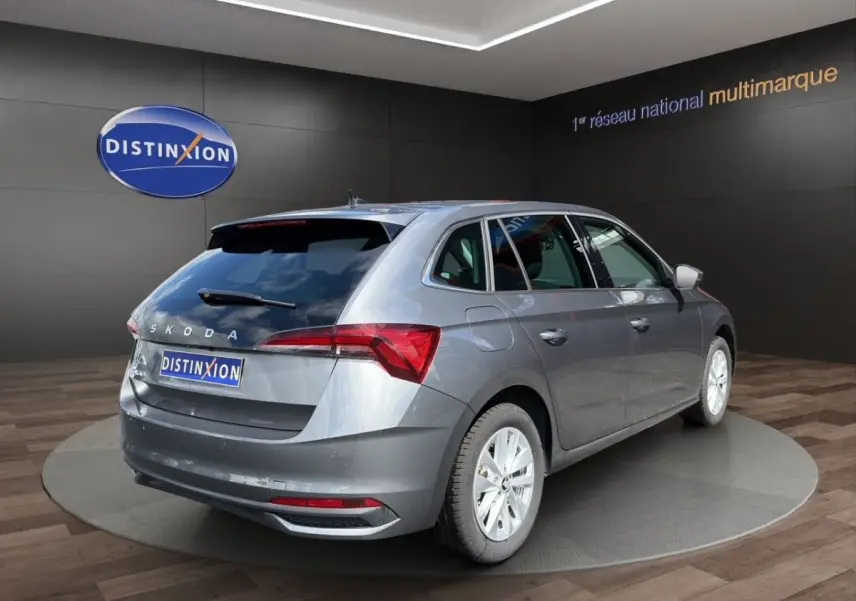 Vue 3/4 arrière droite d'une Skoda Scala gris foncé exposée en showroom avec feux arrière LED et jantes blanches.
