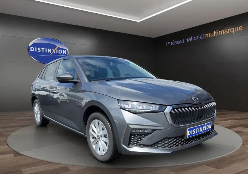 Vue 3/4 avant d'une Skoda Scala gris foncé avec calandre chromée et phares LED, sur fond de showroom Distinxion.
