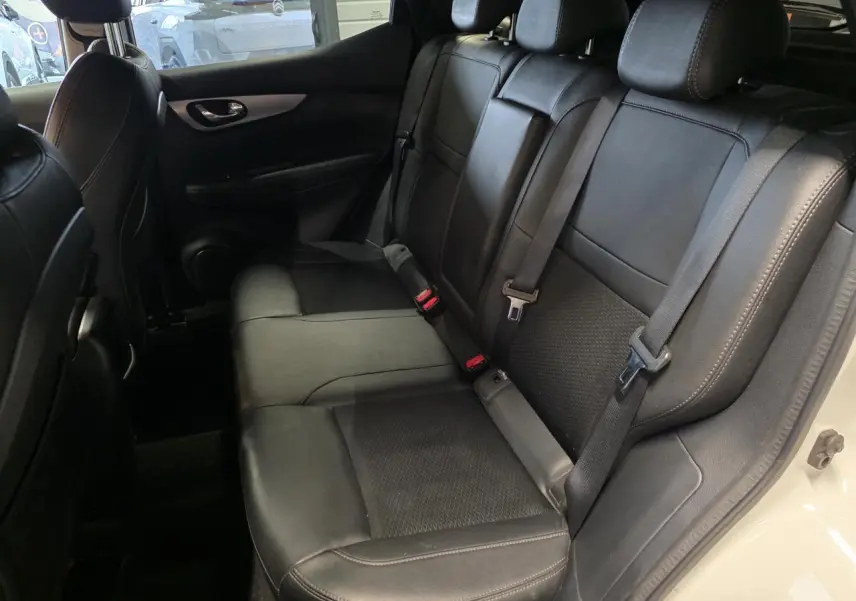Vue intérieure côté droit des sièges arrière en cuir noir du Nissan Qashqai blanc, avec ceintures de sécurité visibles.