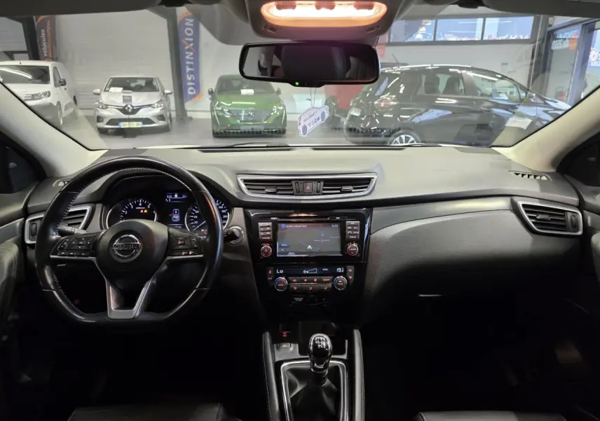 Vue intérieure avant du tableau de bord noir du Nissan Qashqai 1.2 DIG-T 2018 avec volant cuir et écran tactile central.