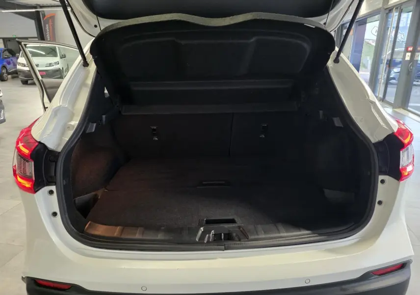 Coffre ouvert vu de l'arrière d'un Nissan Qashqai blanc avec feux arrière LED allumés en intérieur showroom.