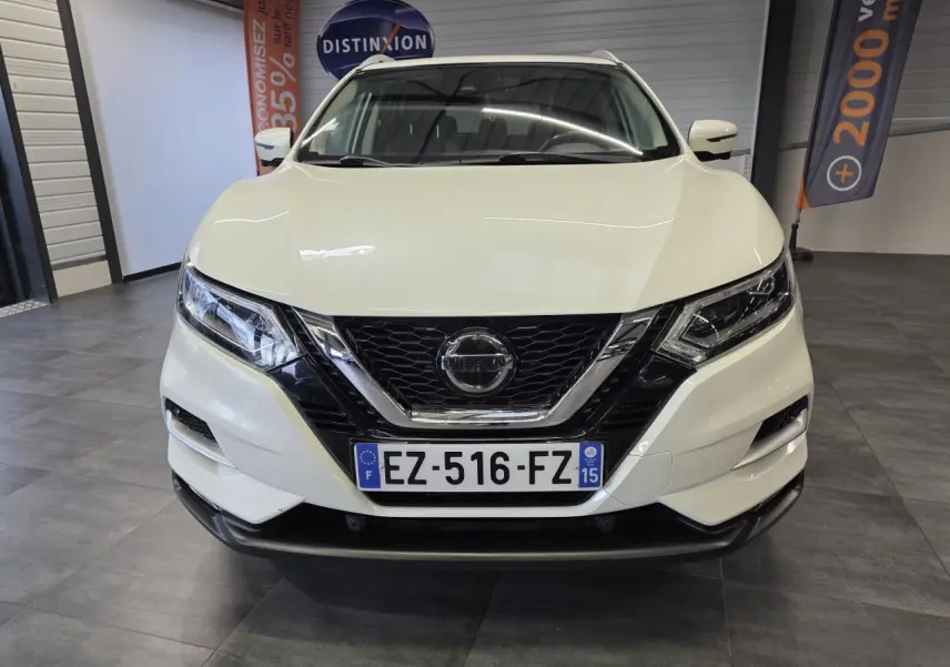 Vue avant d'un Nissan Qashqai blanc avec calandre noire et détails chromés, en intérieur showroom.