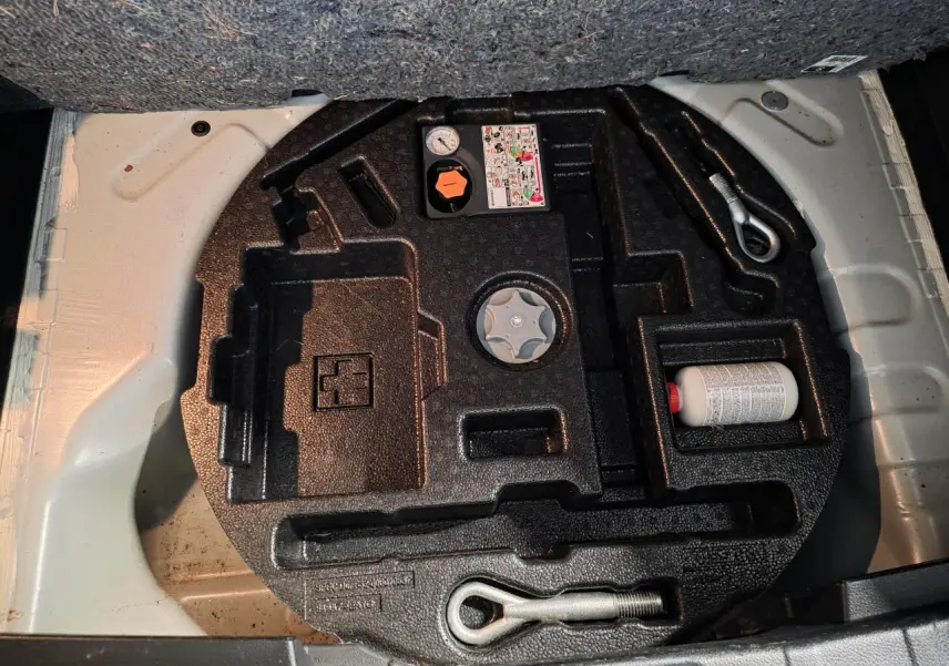 Vue du coffre ouvert montrant le kit de réparation pneumatique dans un Nissan Qashqai blanc 2018.