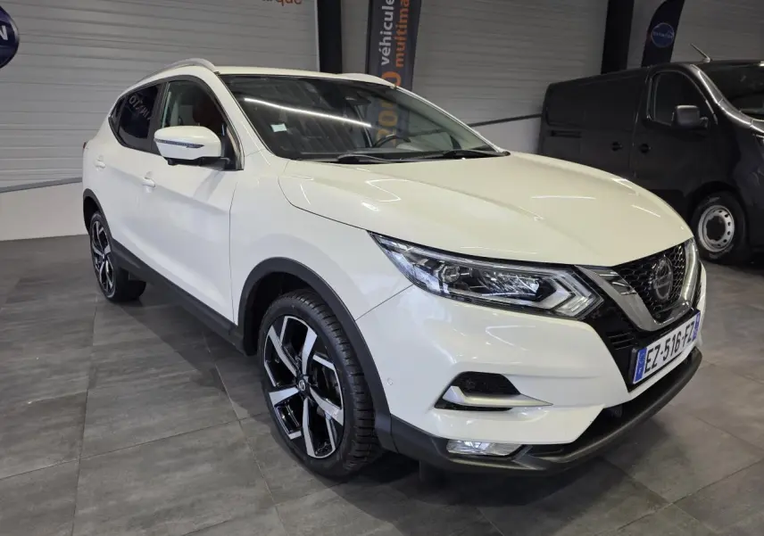 Nissan Qashqai blanc Lunaire en 3/4 avant droit, jantes alliage noires et toit panoramique visible.