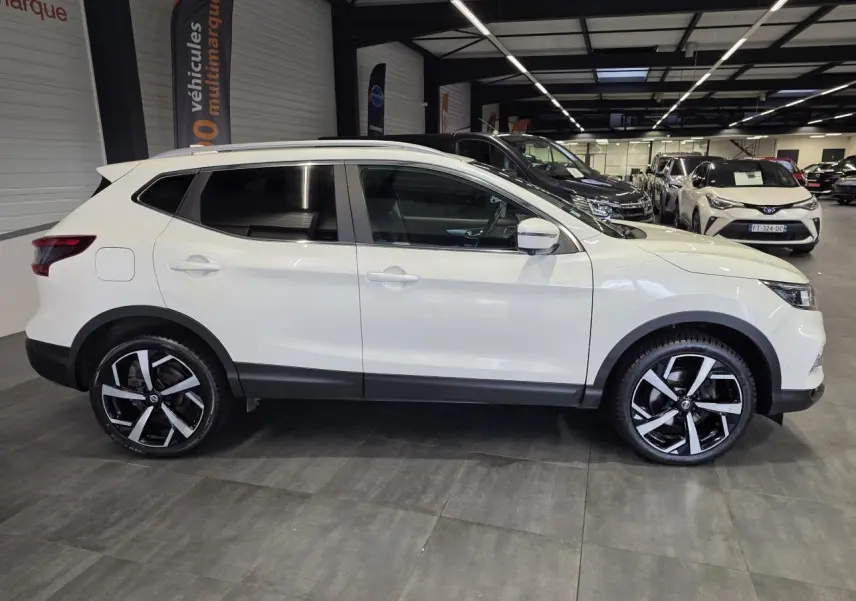 Vue de profil côté gauche d'un Nissan Qashqai blanc avec jantes alliage noires et argent dans un showroom.