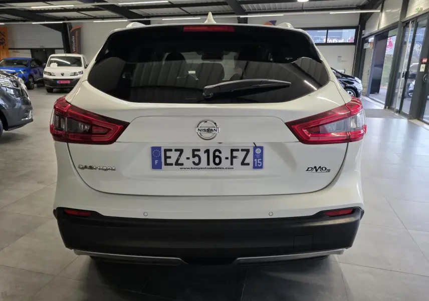 Vue arrière d'un Nissan Qashqai blanc avec feux LED et pare-chocs noir dans un showroom.