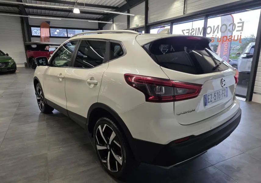 Nissan Qashqai blanc vue 3/4 arrière droit en intérieur avec jantes alliage noires et toit panoramique.