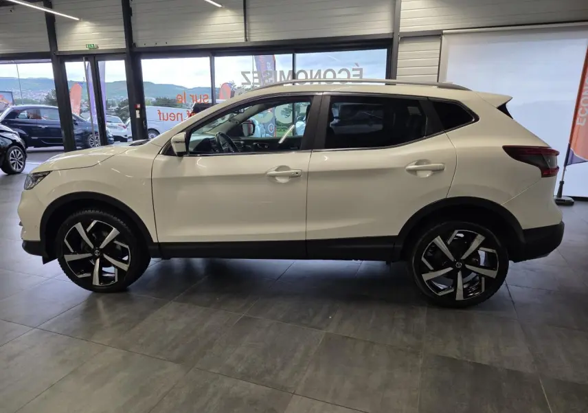 Profil droit du Nissan Qashqai blanc Lunaire avec jantes alliage 19 pouces et toit panoramique en showroom.