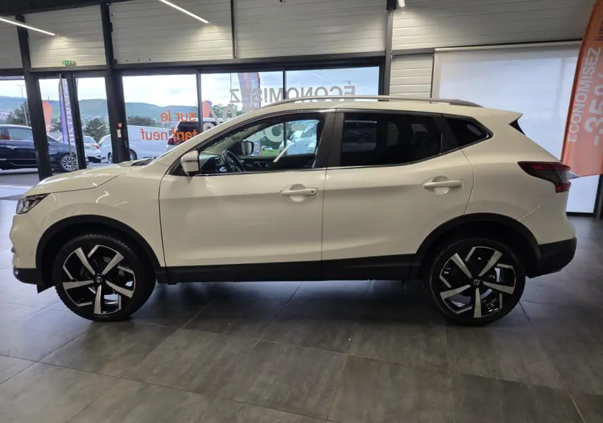 Vue de profil droit du Nissan Qashqai blanc Lunaire avec jantes alliage noires et toit panoramique en showroom.