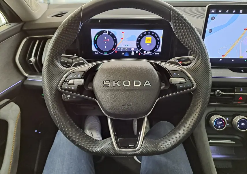 Vue intérieure centrée sur le volant perforé SKODA du KODIAQ 2025 avec tableau de bord numérique et écran tactile latéral.