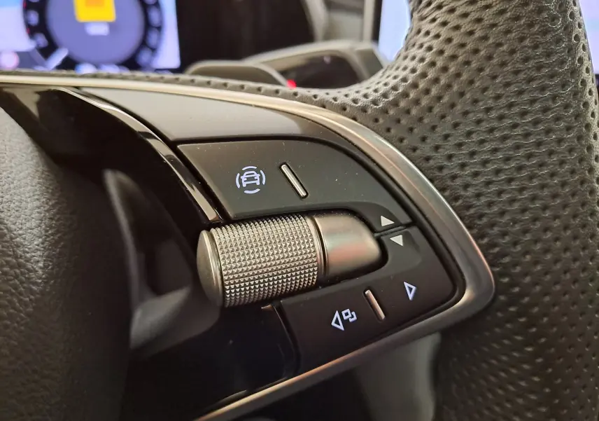 Gros plan sur les commandes du volant perforé du Skoda Kodiaq 2025, avec molette texturée et boutons rétroéclairés.