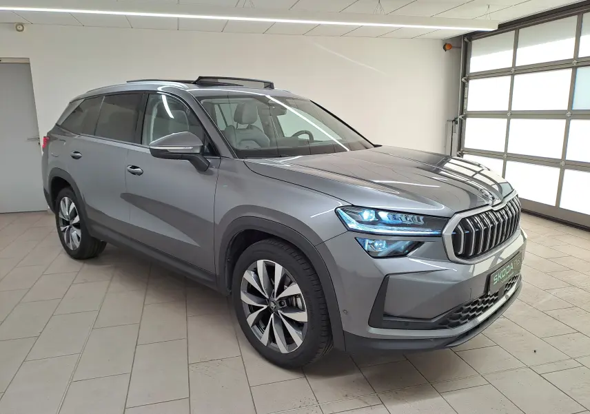 Vue 3/4 avant droit d'un Skoda Kodiaq gris graphite 2025 avec toit panoramique ouvrant et jantes alliage 19 pouces.