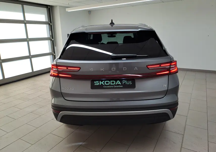 Vue arrière d'un Skoda Kodiaq gris graphite 2025 avec feux LED allumés et vitrage arrière surteinté en intérieur.