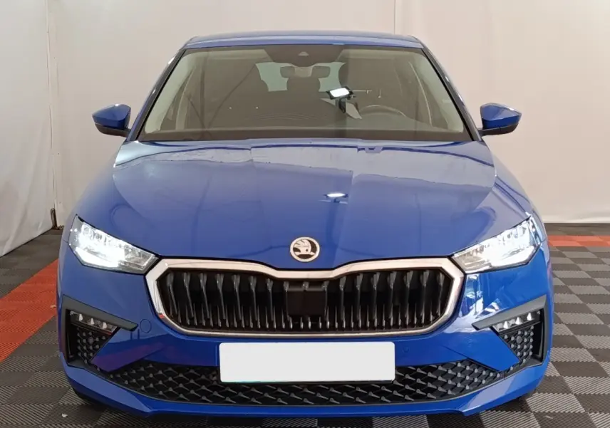 Vue avant d'une Skoda Scala bleu vif avec calandre noire et phares LED allumés dans un intérieur neutre.