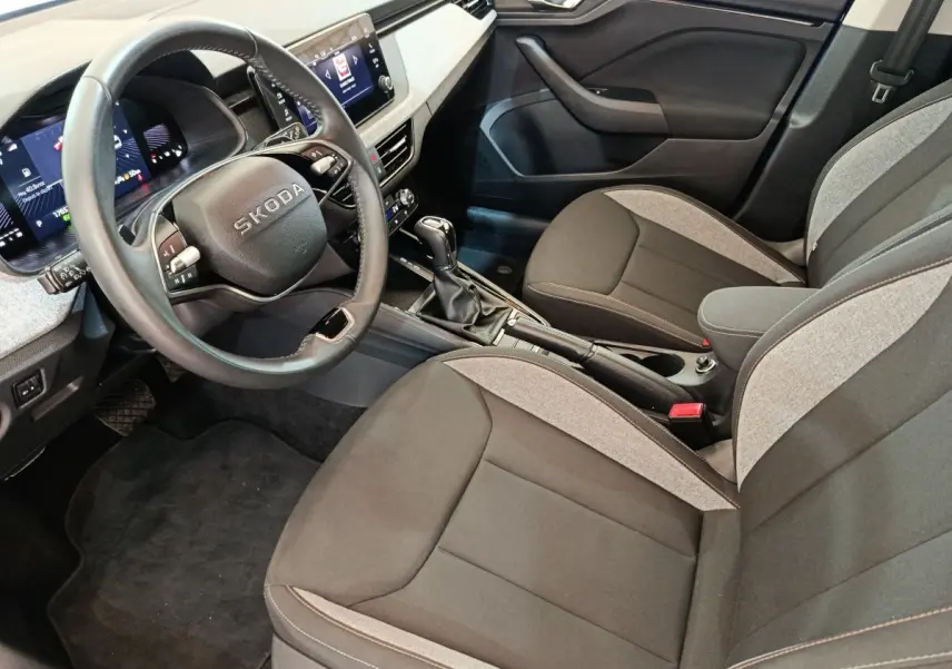 Vue intérieure côté conducteur de la Skoda Scala 2025, volant cuir, sièges tissu bicolore gris et noir, console centrale avec boîte manuelle.