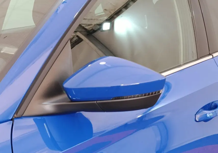 Gros plan sur le rétroviseur côté gauche bleu vif d'une Skoda Scala 2025 avec poignée de porte assortie.