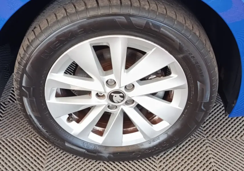Gros plan sur la roue avant droite d'une Skoda Scala bleue, jante alliage argentée avec logo Skoda au centre.