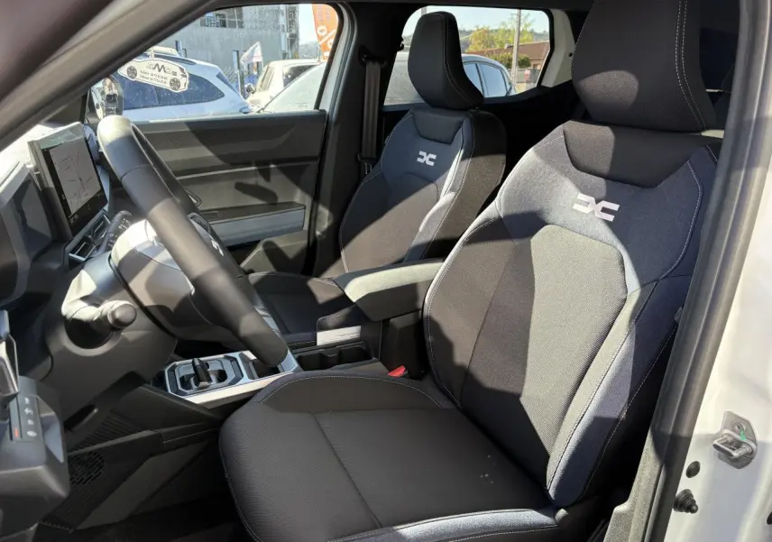 Intérieur du Dacia Duster blanc 2024, vue côté conducteur, sièges en tissu Denim bleu avec logo Dacia.