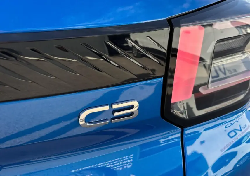 Gros plan sur le logo C3 et le feu arrière droit d'une Citroën C3 bleu vif, soulignant le bandeau noir décoratif.
