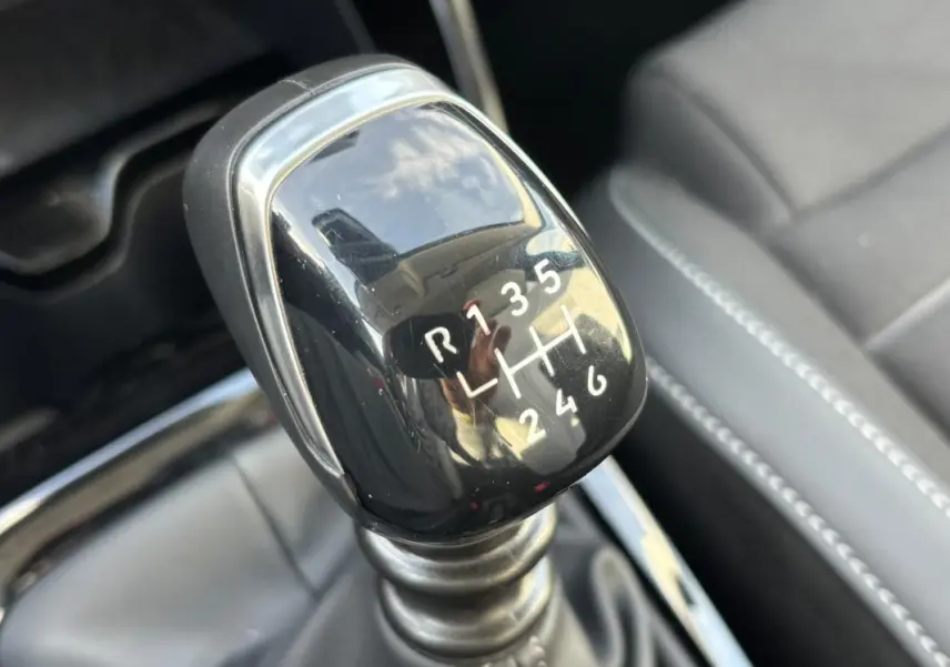 Gros plan sur le levier de vitesses manuel noir de la Citroën C3 Turbo 100 ch, avec sièges en cuir gris en arrière-plan.