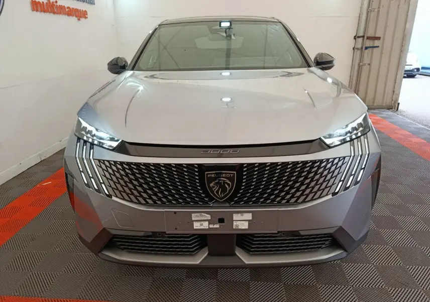 Vue avant frontale du Peugeot 3008 gris clair 2025 avec calandre distinctive et phares LED verticaux allumés.