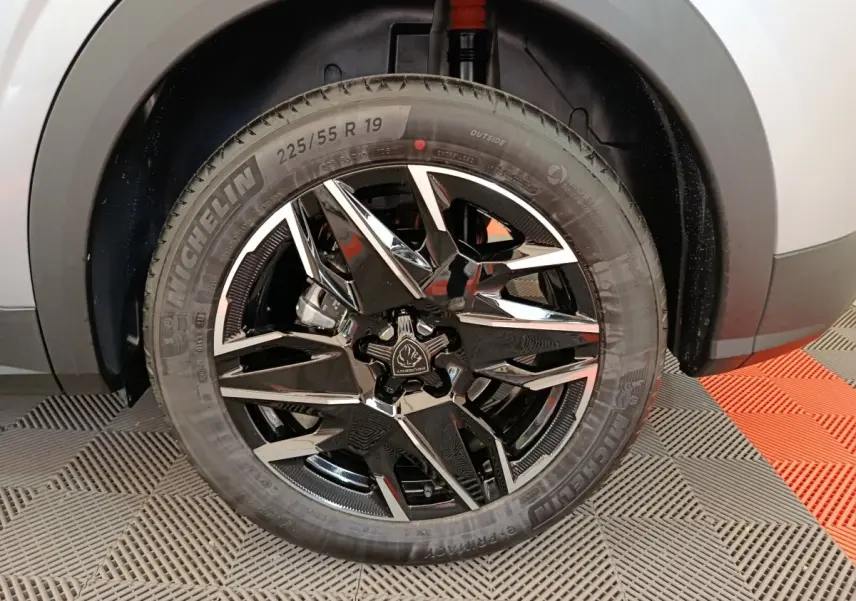 Gros plan sur la roue avant droite du Peugeot 3008 gris clair, mettant en valeur la jante noire brillante au design moderne.