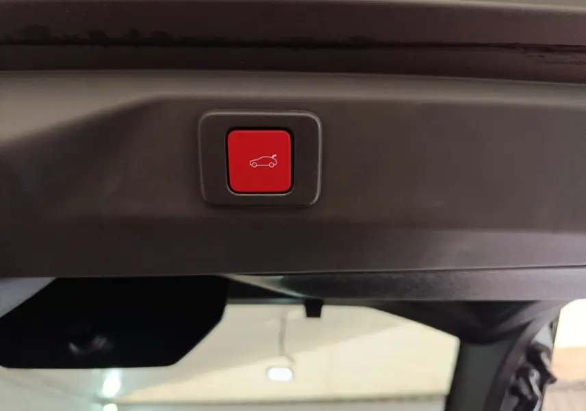 Bouton rouge d'ouverture électrique du coffre sur le hayon intérieur d'un Peugeot 3008 gris clair, vue rapprochée.