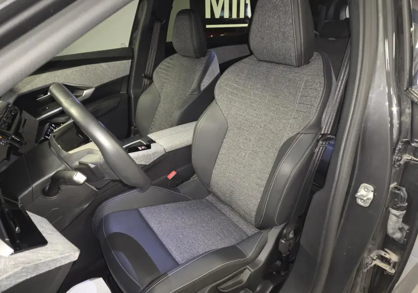 Vue intérieure côté conducteur du Peugeot 5008 gris 2025, sièges tissu gris et cuir noir avec surpiqûres contrastées.
