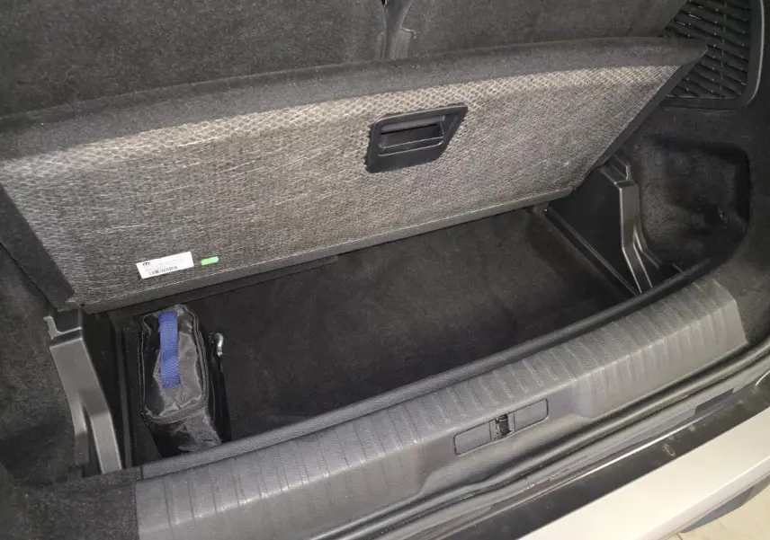 Coffre ouvert en vue plongeante d’un Peugeot 5008 gris, montrant le rangement sous plancher avec trousse noire.