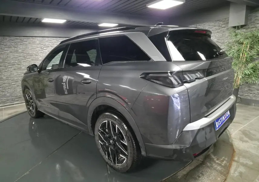 Vue 3/4 arrière droite d’un Peugeot 5008 gris métallisé avec jantes alliage noires et bandeau noir laqué entre feux arrière.