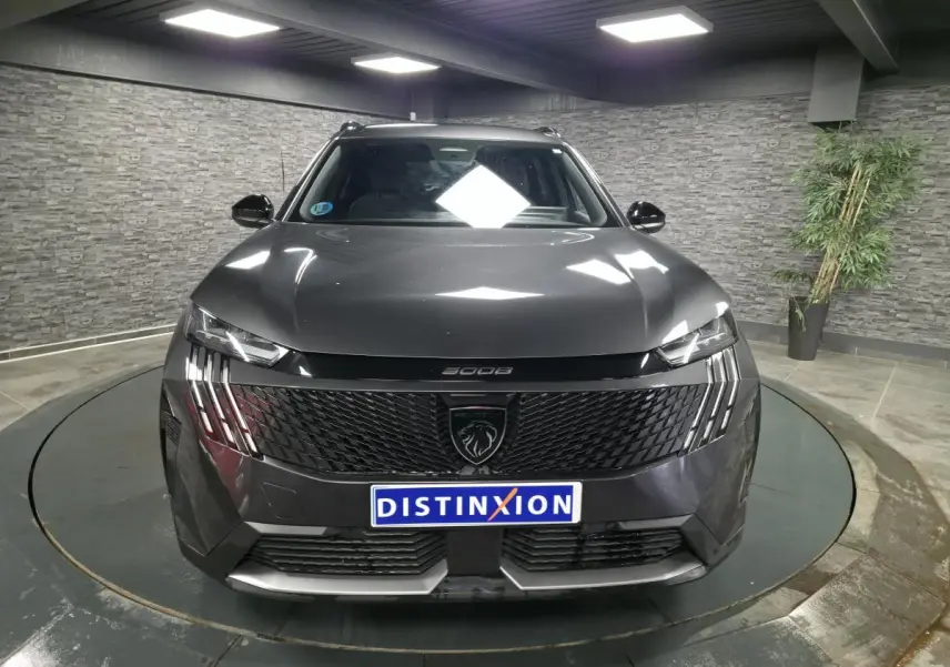 Vue frontale d'un Peugeot 5008 gris métallisé 2025 avec calandre noire et feux LED à griffes dans un showroom.