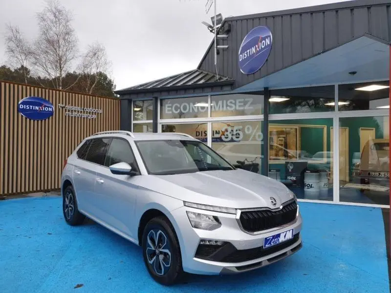 Vue 3/4 avant gauche d’un Skoda Kamiq gris diamant métallisé avec jantes alu et calandre noire devant un showroom.
