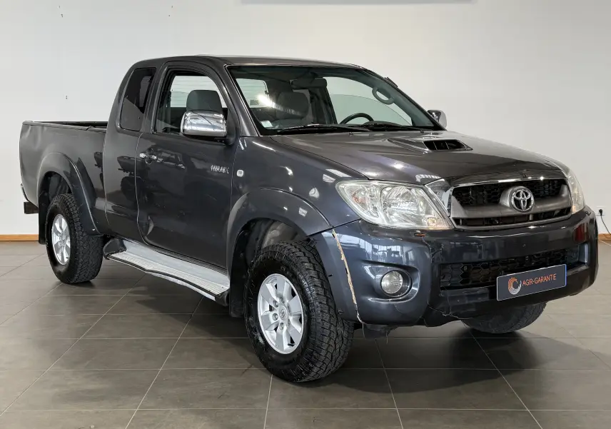 Toyota Hilux X-Tra Cabine gris vue 3/4 avant droit, avec calandre chromée et marchepieds latéraux visibles.
