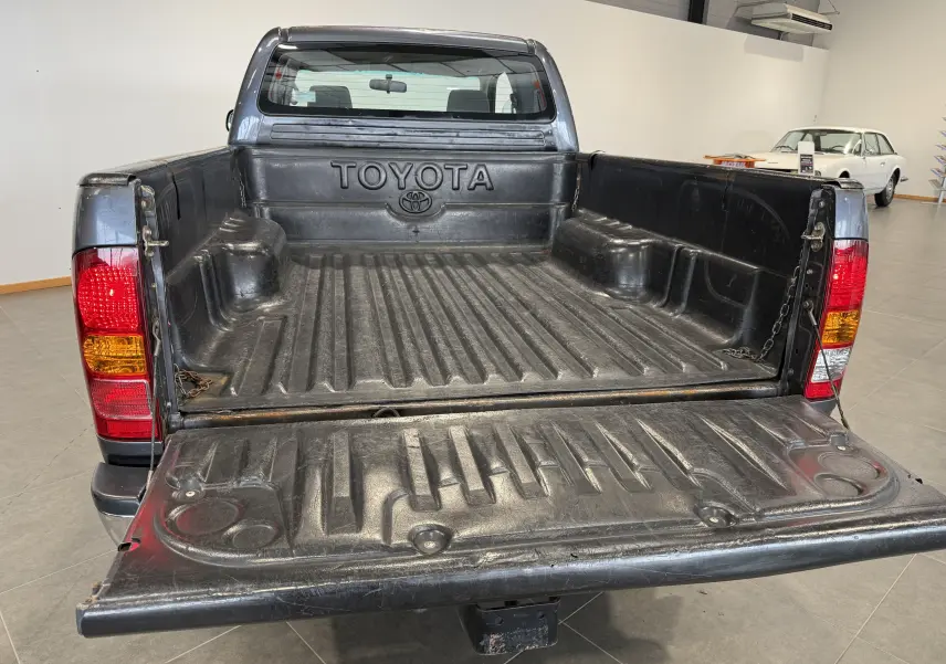 Vue arrière ouverte du Toyota Hilux X-Tra Cabine gris 2009, mettant en valeur la benne et les feux arrière rouges et orange.