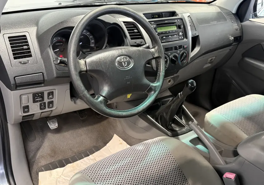 Vue intérieure côté conducteur du Toyota Hilux X-Tra Cabine gris 2009, montrant le volant, tableau de bord et levier de vitesses manuel.