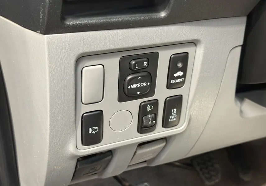 Gros plan sur les commandes grises du tableau de bord du Toyota Hilux X-Tra Cabine 2009, avec boutons de réglage des rétroviseurs et sécurité.