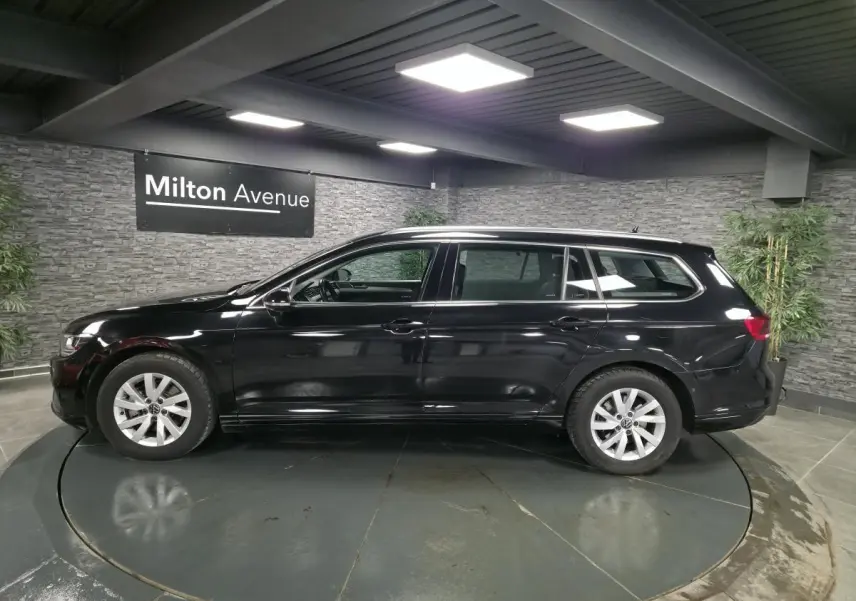 Volkswagen Passat SW noire vue de profil côté gauche dans un showroom avec éclairage intérieur.