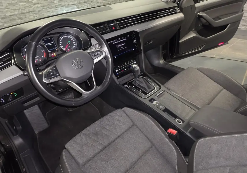 Vue intérieure côté conducteur de la Volkswagen Passat SW 2024, volant cuir noir et sièges tissu gris.