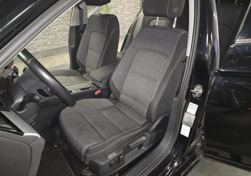 Vue intérieure côté conducteur de la Volkswagen Passat SW 2024 noire, sièges tissu gris avec surpiqûres blanches.