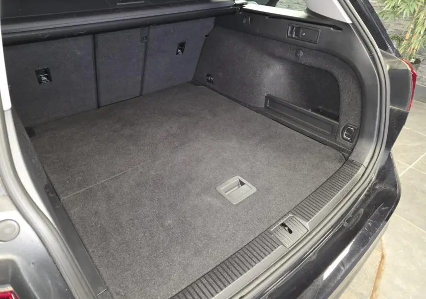 Coffre ouvert d'une Volkswagen Passat SW noire, montrant l'espace de chargement et les finitions intérieures en tissu gris.