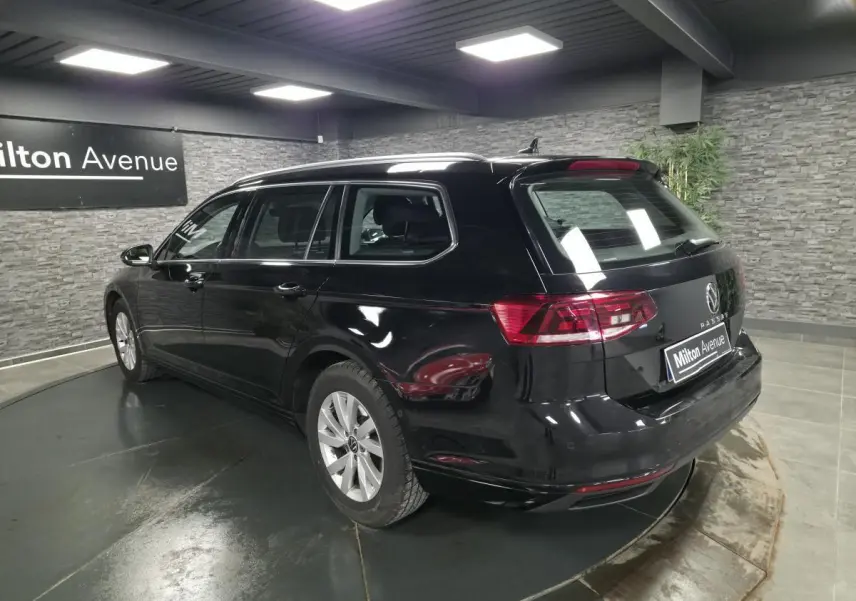 Volkswagen Passat SW noire vue 3/4 arrière droit dans un showroom avec mur en pierre grise.